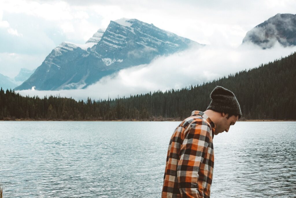 man in orange and white plaid dress shirt standing near lake during daytime